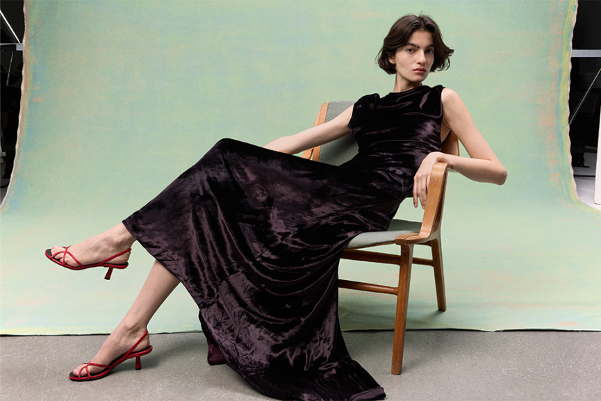 female model in black dress in wooden chair with green background